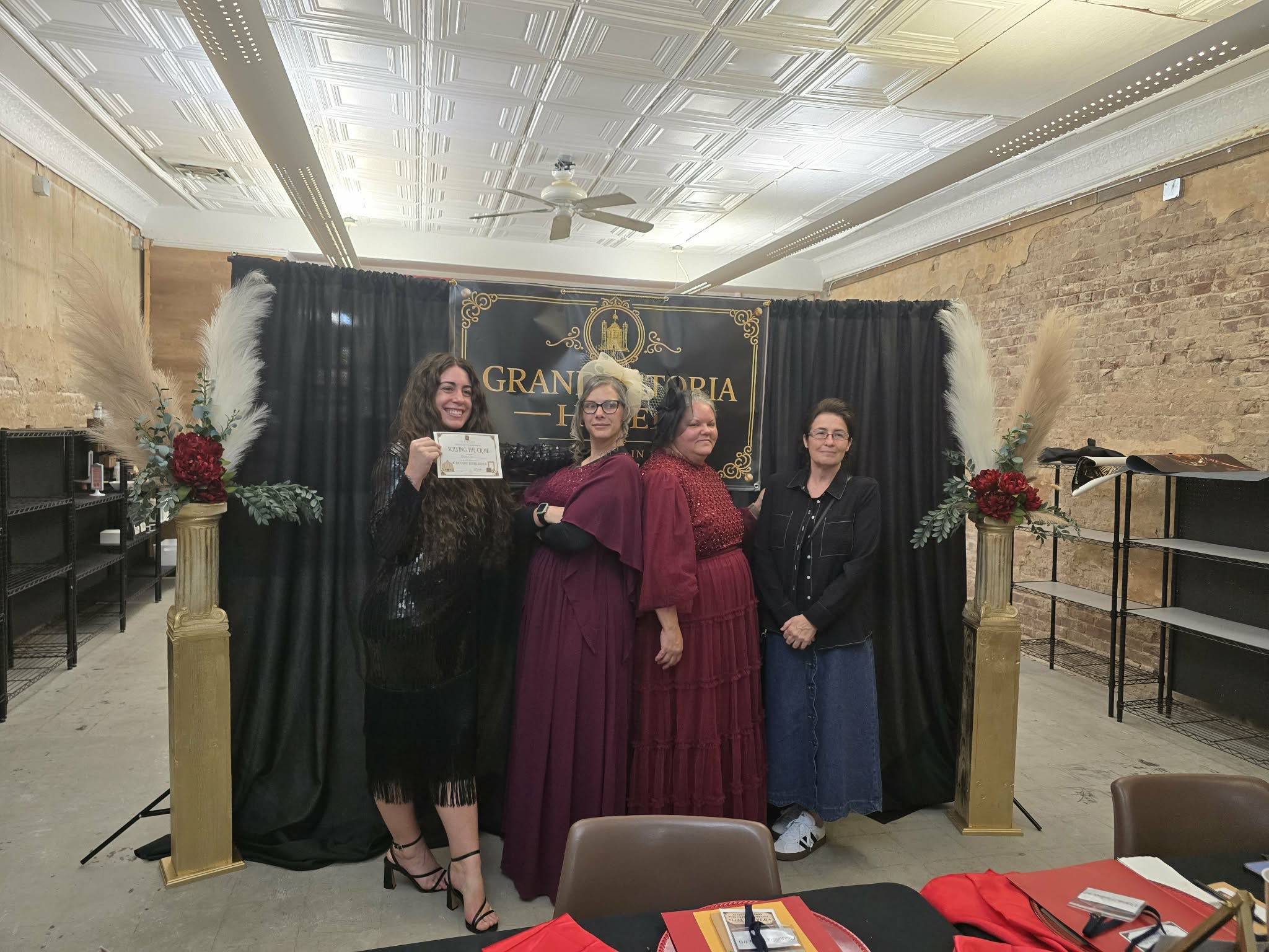 Four guests in 1920s dress posing with a Solving the Crime certificate in front of the Grand Astoria Hotel backdrop.